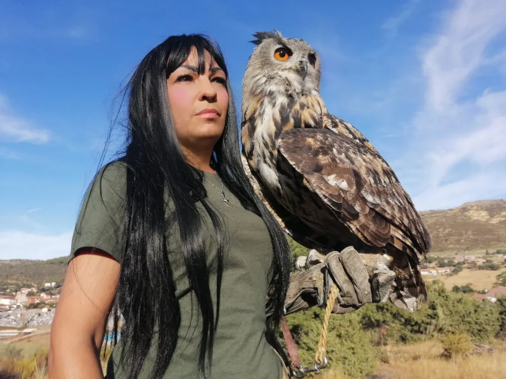 Mujer con búho real sobre el guante en paisaje natural.